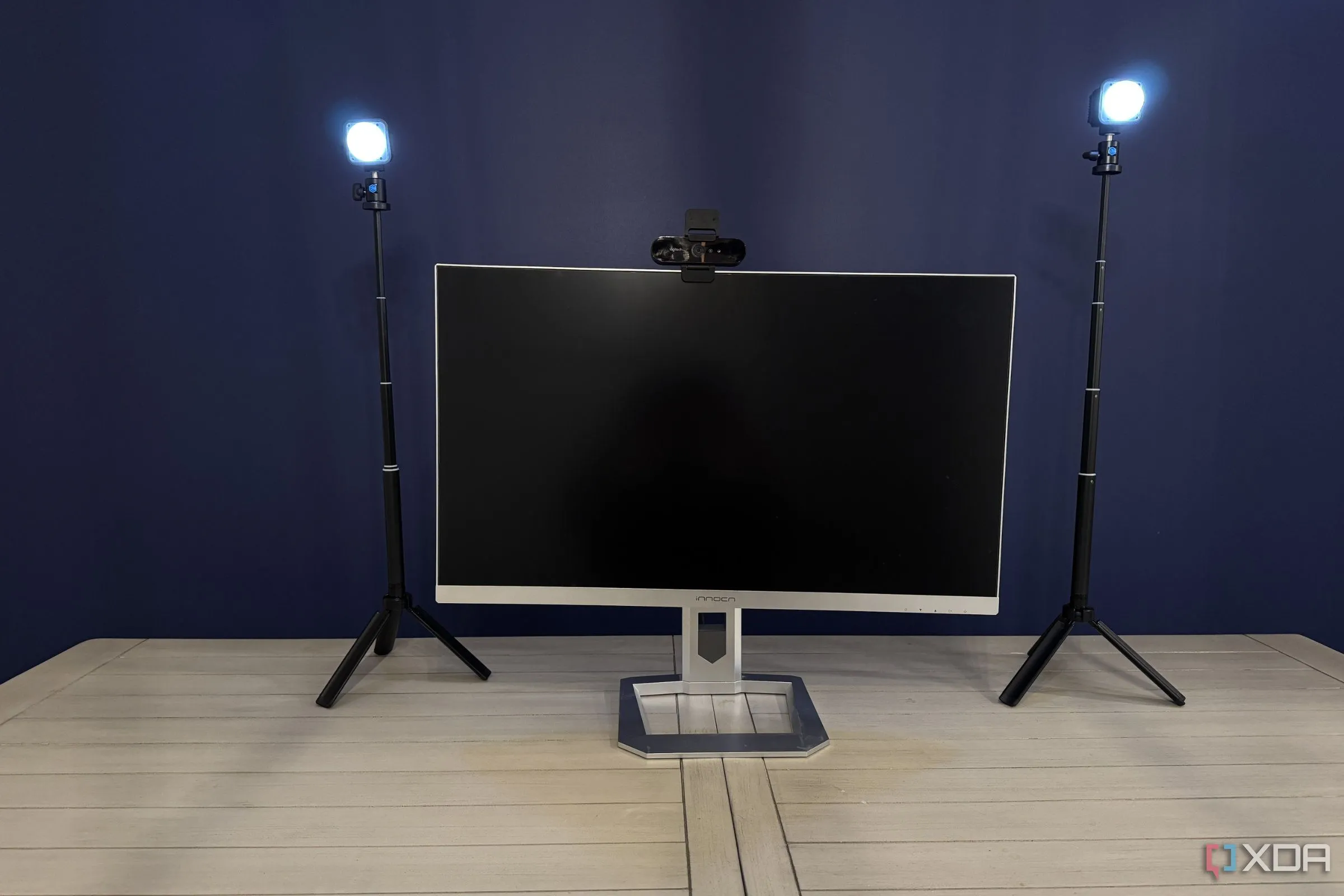 Bàn làm việc lộn xộn với webcam và đèn livestream được gắn tạm trên màn hình, dây cáp không gọn gàng trước khi sử dụng Monoblocc Monitor Rig.