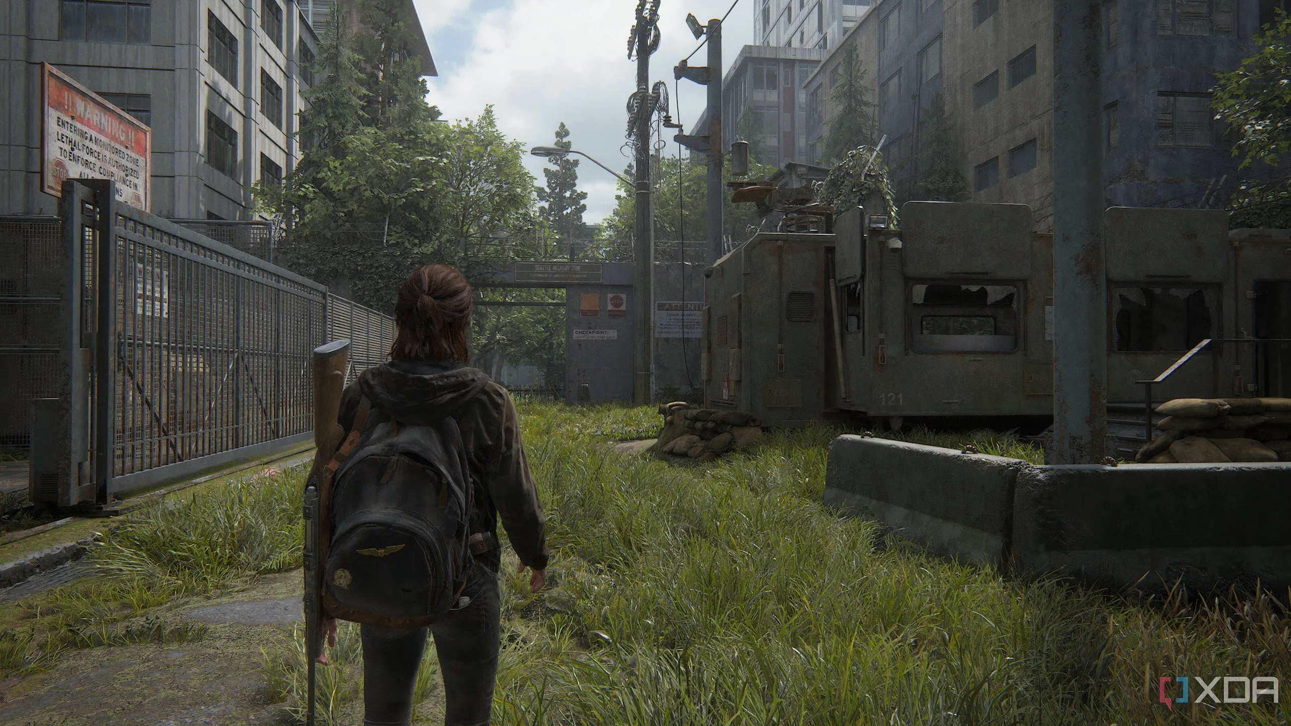 Ellie di chuyển qua khu căn cứ quân sự WLF trong The Last of Us Part II Remastered.