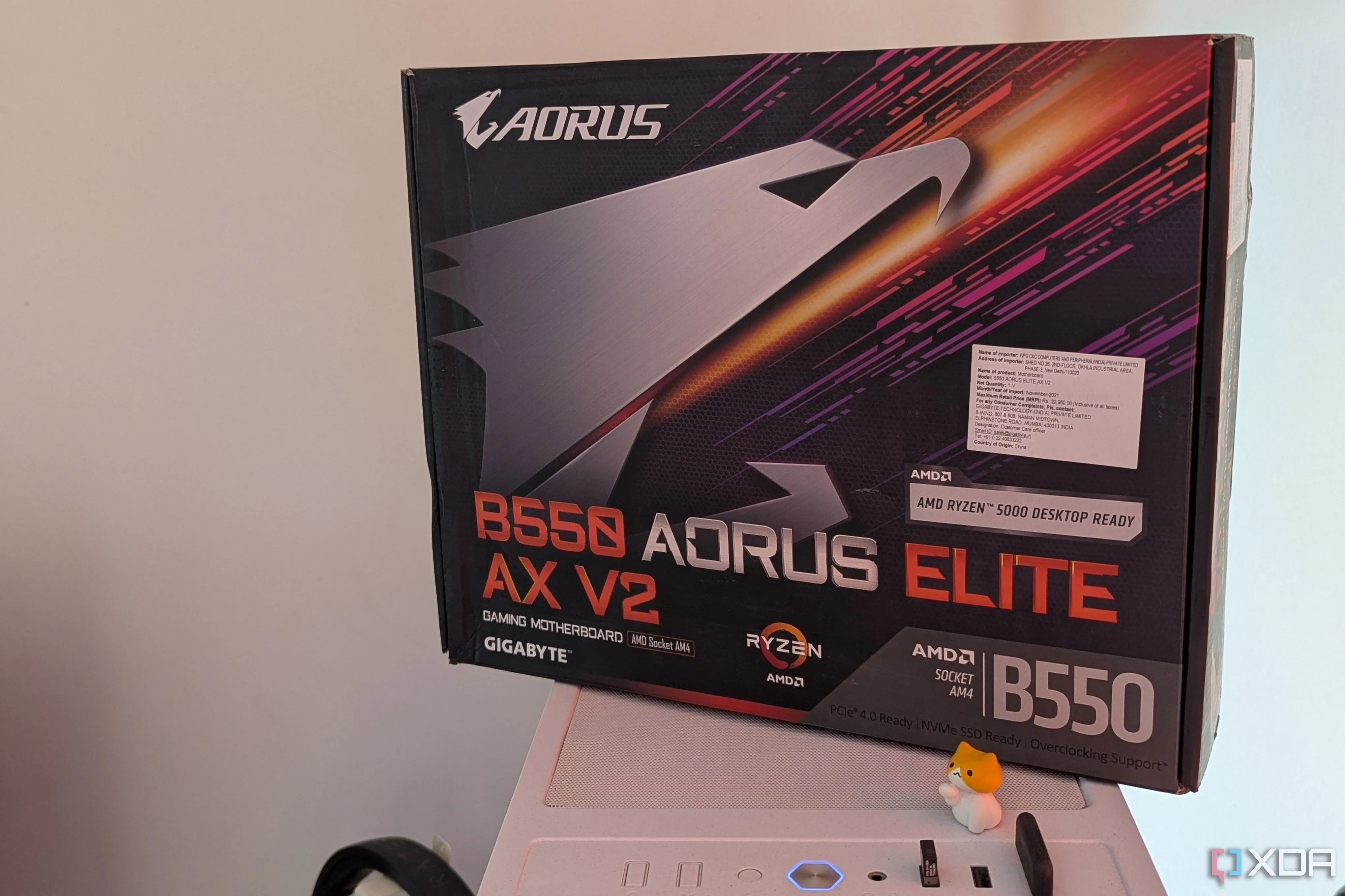 Hộp bo mạch chủ Gigabyte đặt trên vỏ máy tính màu trắng, cạnh đó là bo mạch chủ Gigabyte B550 Aorus Elite AX V2