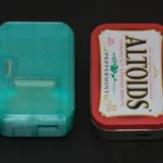 Kích thước Pi Tin so với hộp Altoids và các vật dụng khác, minh họa sự nhỏ gọn của máy chơi game cầm tay Raspberry Pi