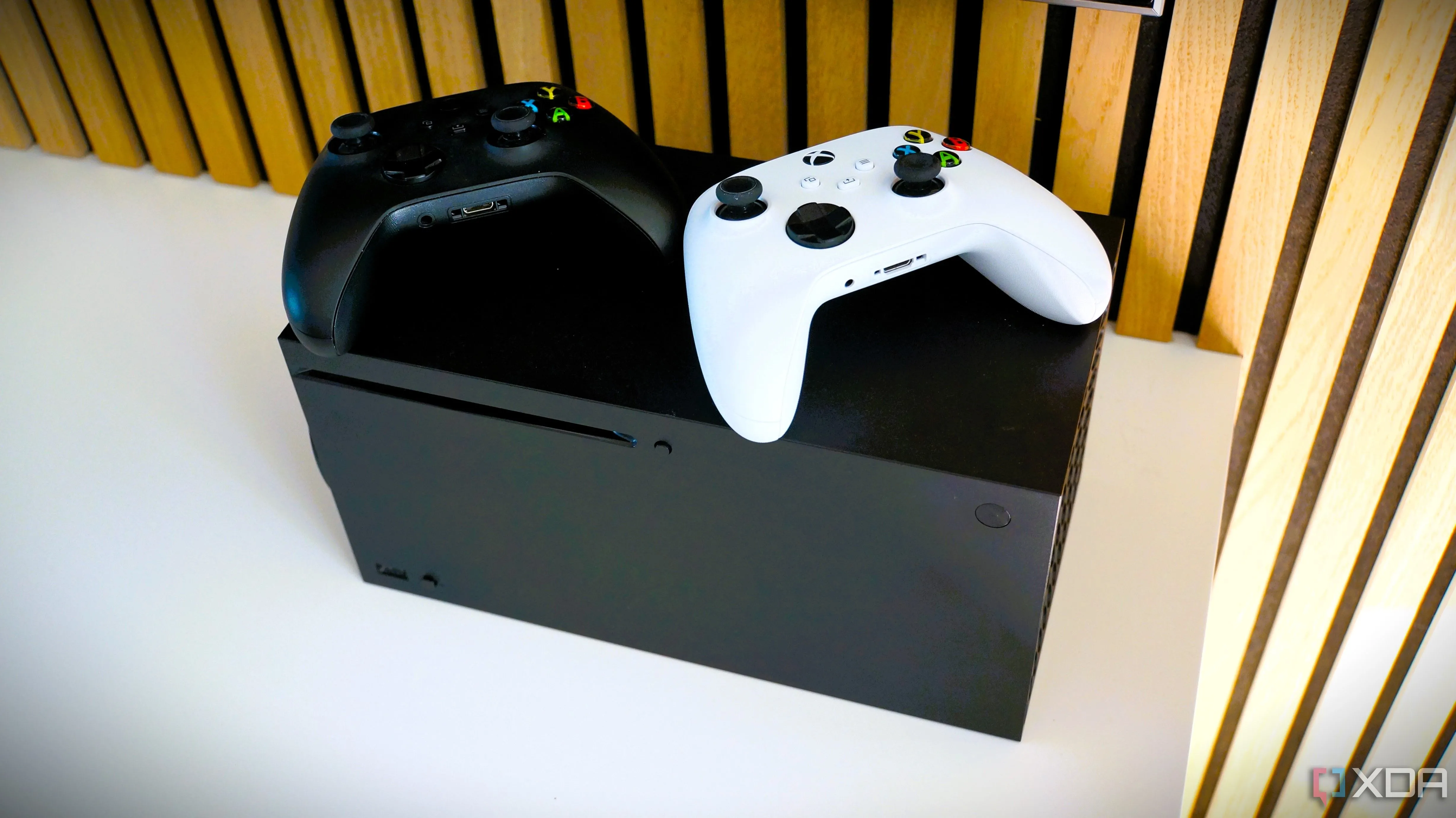 Máy chơi game Xbox Series X màu đen cùng với hai tay cầm không dây, đại diện cho khả năng tương thích ngược và Smart Delivery của Xbox